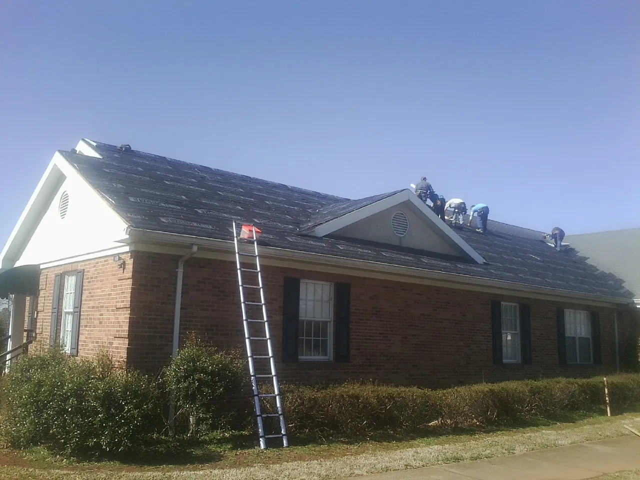 Crew tearing shingles off a brick ranch roof with a ladder set — Emergency Roof Repair work by our crew in Paige