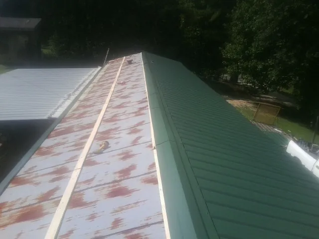 Old rusted panels beside newly installed green metal roofing — Wind Damage Roof Repair by Roofing Brothers in Paige