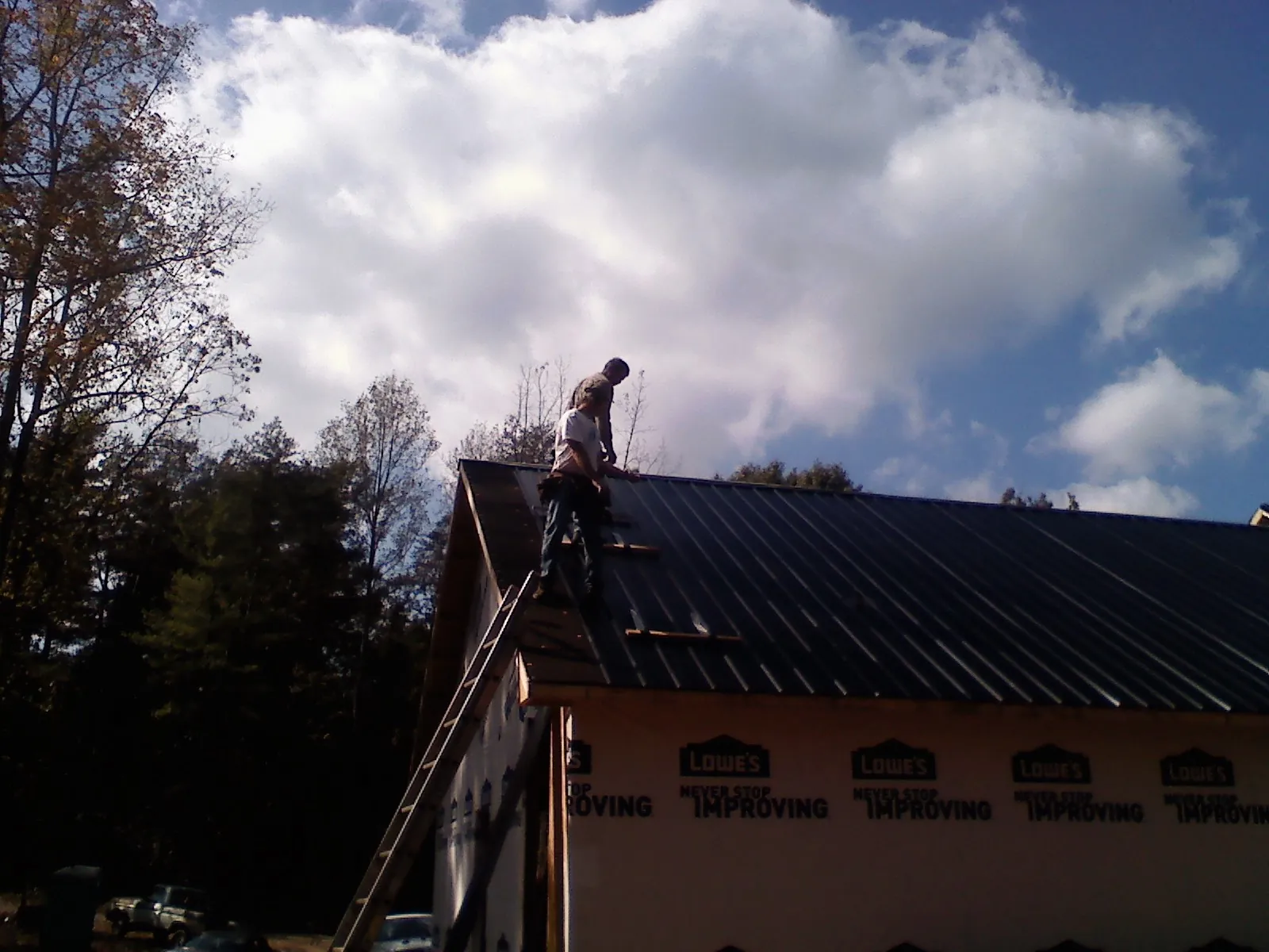 Roofer fastening dark metal panels high against a cloudy sky, from a Roof Inspection job in Paige