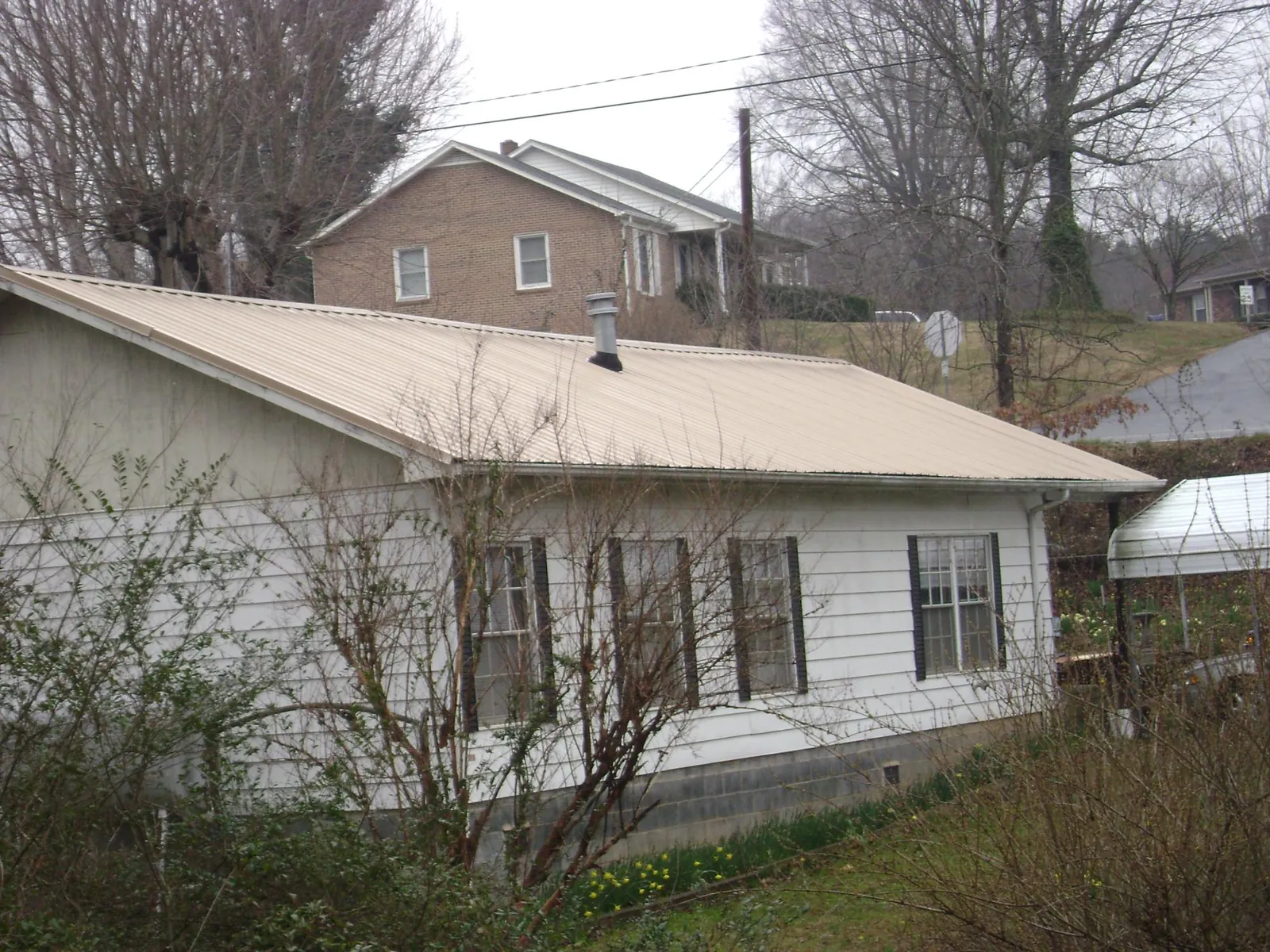 Tan metal roof on a white sided house set into a hillside — Commercial Roofing by Roofing Brothers in Paige